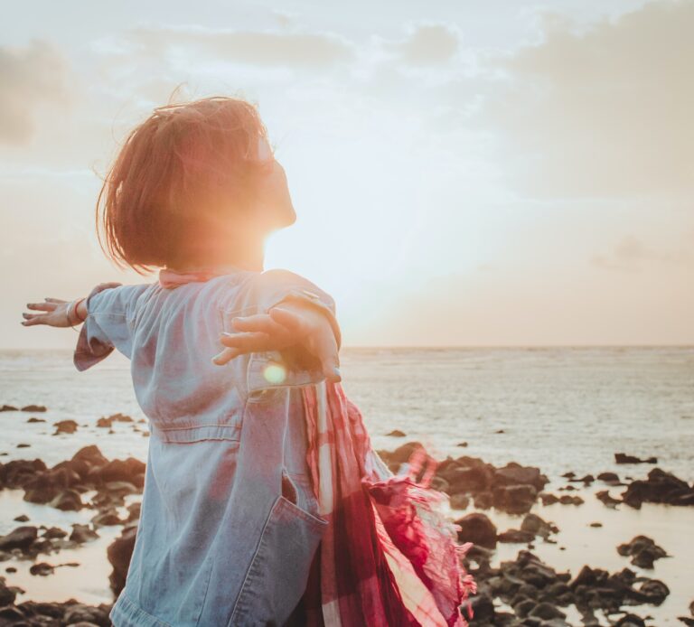 A woman with outstretched arms as the sun rises over the sea