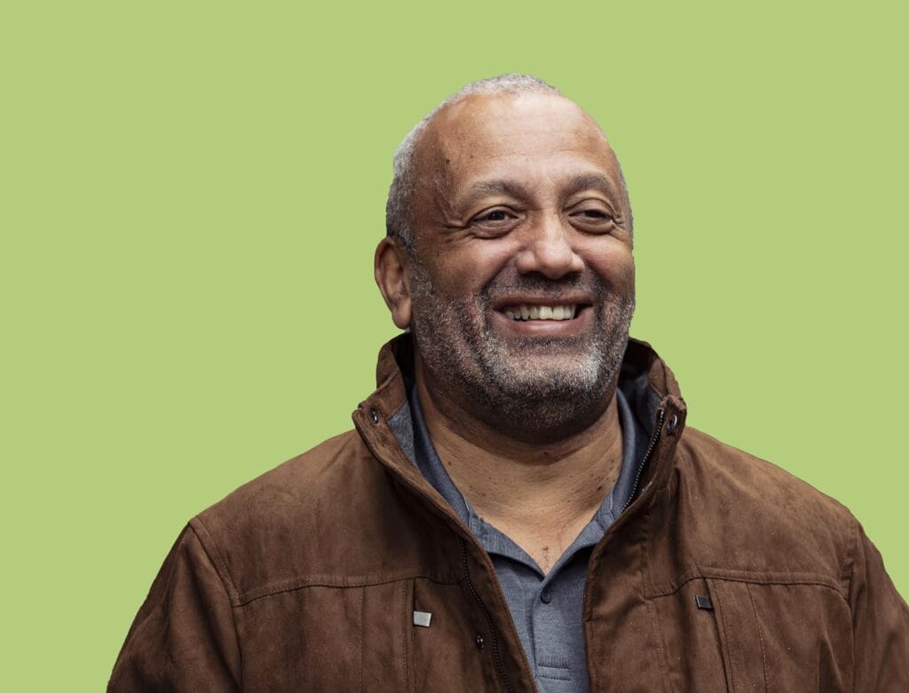 Man standing smiling in front of a light green background.
