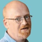 A bald man with glasses and a blue shirt.