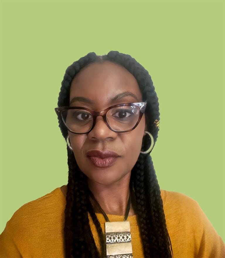 Woman with glasses and mustard coloured jumper in front of a green background