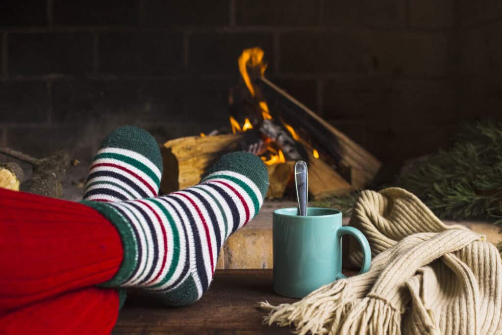 Person wearing red leggings and white, green and red stripey socks in front of a fire with a mug of a hot drink