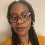 Woman wearing a mustard jumper, brown glasses and hoop earrings