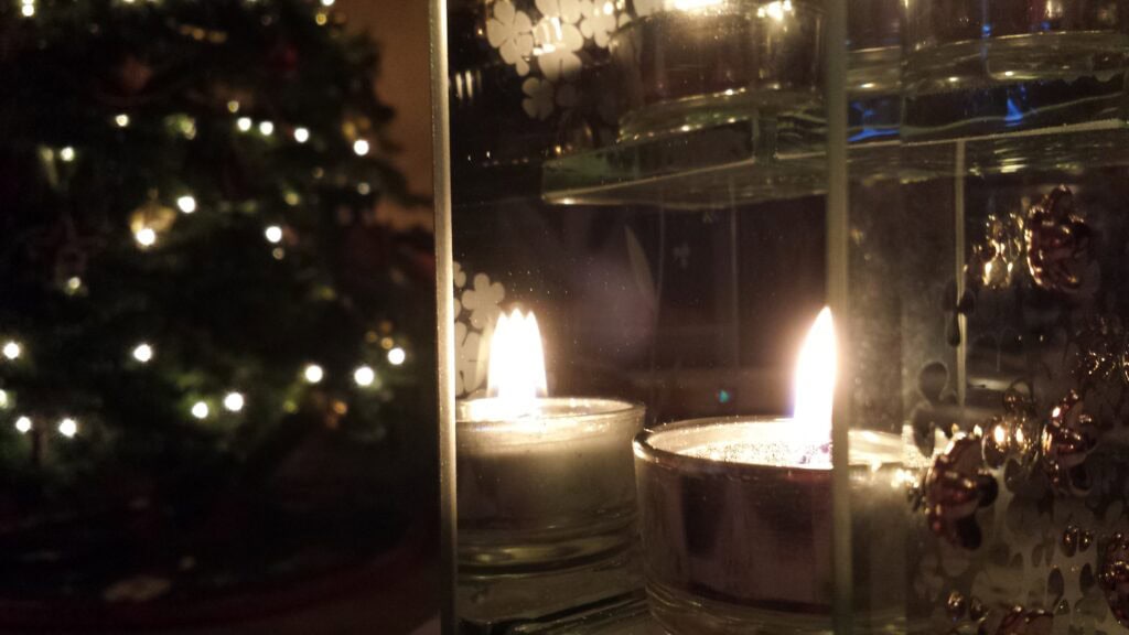 Candle and Christmas tree in background, muted tones